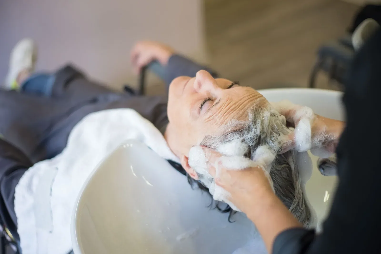 Persona aplicando shampoo en el cuero cabelludo durante el lavado del cabello
